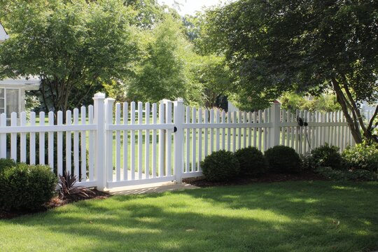 Pristine white vinyl picket fence lining a manicured green lawn in a suburban backyard