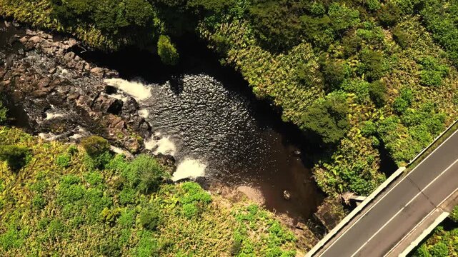 Aerial view of a small river and waterfall flowing under a bridge in lush Flores, Portugal
