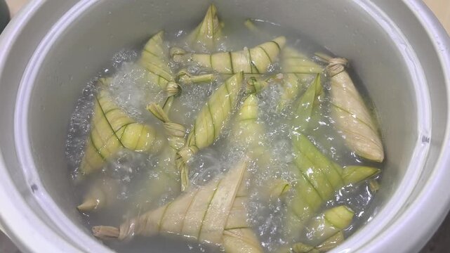 Traditional ketupat palas are boiling gently in a large pot. The glutinous rice cakes are wrapped tightly in fan palm leaves. They are being prepared for a festive celebration.