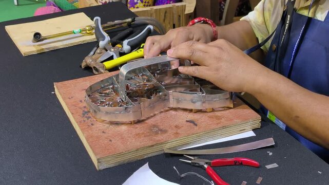 A craftsman creates a copper batik stamp. This traditional Malay art tool is dipped in hot wax to stamp patterns onto fabric. It saves time compared to hand-drawing.