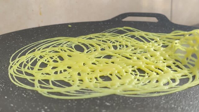 A chef expertly prepares traditional Malay roti jala. This net-like crepe is made from flour batter. It features a bright yellow color and is perfectly paired with savory curry.