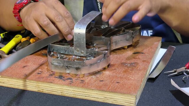 A craftsman creates a copper batik stamp. This traditional Malay art tool is dipped in hot wax to stamp patterns onto fabric. It saves time compared to hand-drawing.