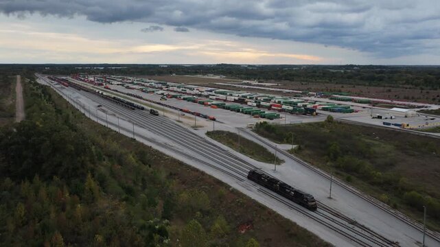 Expansive intermodal rail terminal with trains and cargo storage areas, drone pullback at sunset with freight train on edge