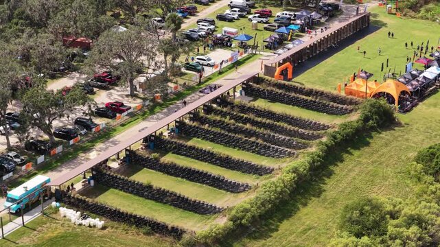 Aerial overview of parallel shooting lanes and safety berms beside expo grounds as people walk on open grass visiting booths