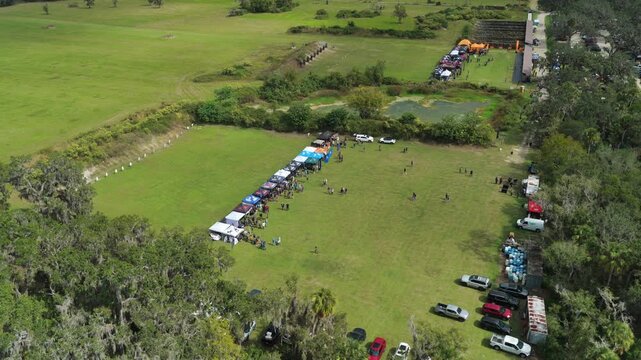 High aerial pullback orbit of shooting range event grounds, car parking and vendor area, drone