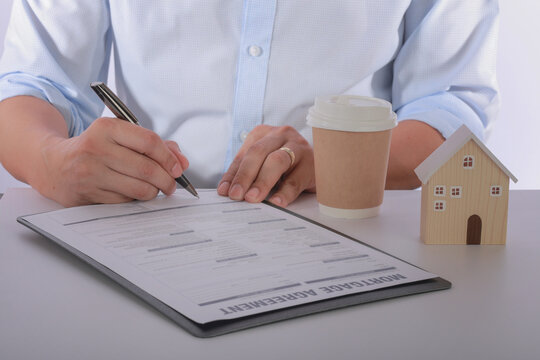 Focused and determined buyer signing real estate contract during successful home loan approval process with wooden house model
