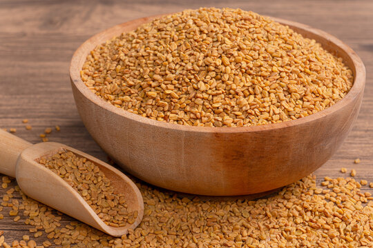 Heap of raw fenugreek seeds in wooden bowl with wooden scoop on rustic wooden surface