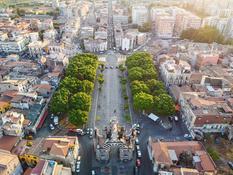 Aerial view of the historic Porta Garibaldi arch surrounded by lush trees and urban buildings in the city center of Catania, Sicily, Italy.