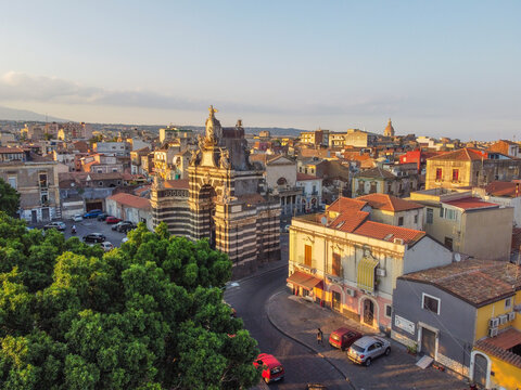Aerial view of the historic Porta Garibaldi archway surrounded by traditional Sicilian rooftops, narrow streets, and lush green trees in Catania, Sicily, Italy.