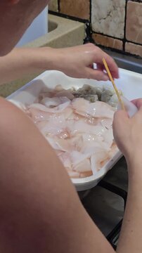 Woman hands skewering raw fresh squid on wooden stick from plastic tray preparing traditional delicious seafood skewers inside domestic kitchen in Italy cooking concept. Video 4k