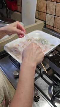 Woman hands skewering raw fresh squid on wooden stick from plastic tray preparing traditional delicious seafood skewers inside domestic kitchen in Italy cooking concept. Video 4k