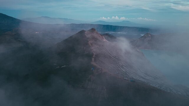 Stunning aerial drone view of Kawah Ijen volcano featuring its iconic crater, volcanic ridge, sulfur smoke, and turquoise crater lake during sunrise in East Java, Indonesia. Dramatic volcanic landscap