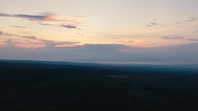 Beautiful aerial drone footage capturing a peaceful sunrise over the mountainous landscape of East Java, Indonesia. Soft golden light, colorful clouds, distant hills, and a tranquil horizon create a b