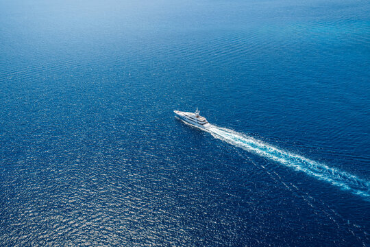 High aerial view of a lmodern uxury yacht cruising over the blue ocean with speed