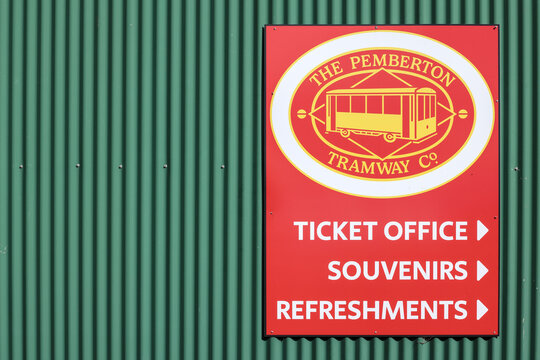 Pemberton, Western Australia, Australia - May 16 2026: Red, yellow sign, Pemberton Tramway Company mounted on a green corrugated wall. Directing travel visitors to ticket office, souvenirs, tourism
