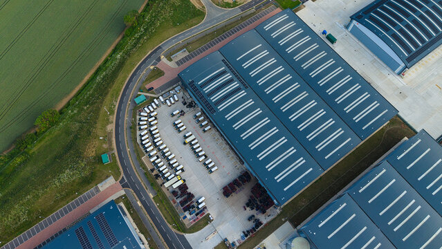 Aerial view of a large logistics warehouse facility with solar panels on the roof and rows of delivery vans parked in the yard in Biggleswade, England, United Kingdom.