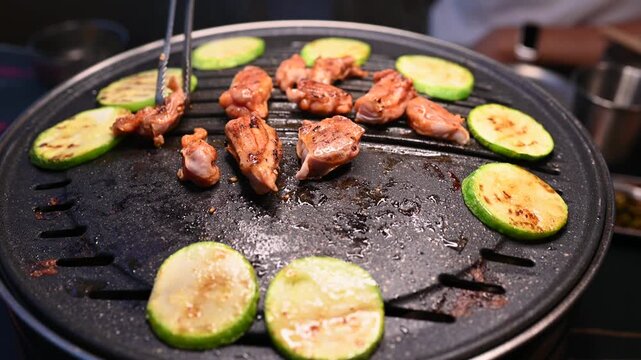 Grilling Meat and Vegetables on a Hot Plate with Tongs in a Restaurant Setting