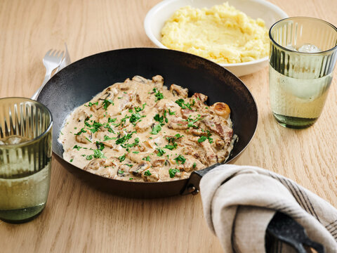 Creamy mushroom dish with parsley, served alongside mashed potatoes and refreshing beverages for a home-cooked meal