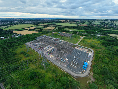 Aerial view of Wymondley Substation with complex electrical infrastructure, transformers, and switchgear surrounded by lush green fields in Saint Ippolyts, England, United Kingdom.