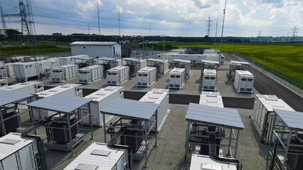 Battery energy storage system with multiple container units and connecting equipment providing electrical power to a high voltage substation and electricity transmission lines © Dark Artistic