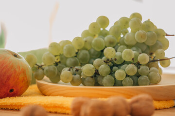 Fototapeta premium Fresh green grapes, red and green apples, and walnuts arranged on a wooden tray — perfect for healthy eating, nutrition, and organic lifestyle concepts