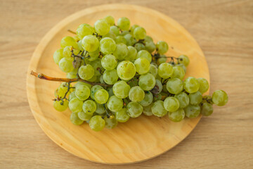 Fototapeta premium Fresh green grapes on a round wooden plate, shot from above on a light wood surface. Perfect for healthy eating and organic food concepts