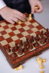 A close-up of white and black wooden chess pieces on a board. A boy's hands arrange the pieces on the board. © Natalya Likhina