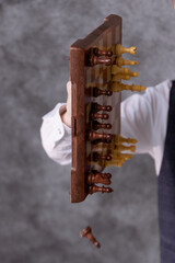 A close-up of chess pieces on a board. A boy's hand holds the board vertically, and the pieces begin to fall.  © Natalya Likhina