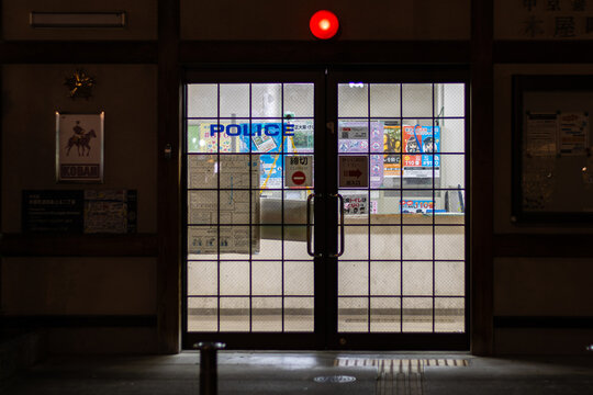 Kyoto, Japan April 18, 2026 entrance door of japanese koban police station at night with illuminated interior visible through glass panels and red warning light above