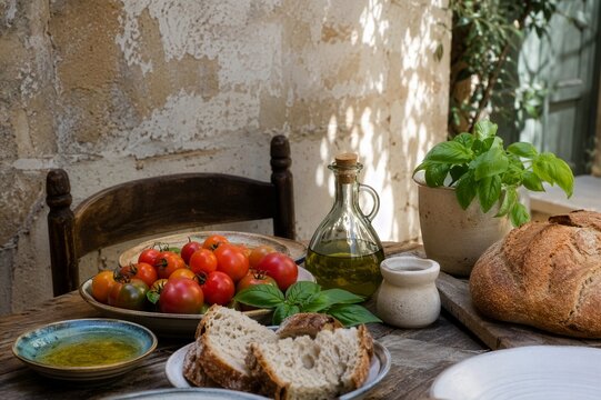 Rustic Mediterranean table with bread, olive oil, fresh tomatoes and basil in a sunlit local courtyard