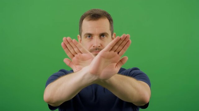 Man making stop gesture with arms crossed in front of green screen background during presentation