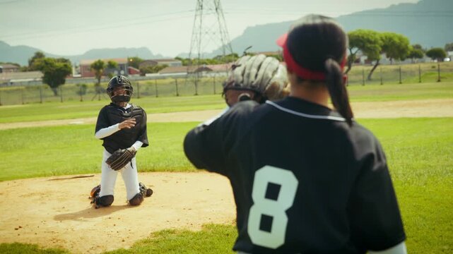 A pitcher throws the ball to a catcher, both dressed in uniform, practicing on a baseball field. The catcher skillfully receives the pitch during their training session.