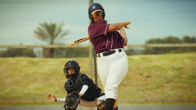 A focused baseball batter powerfully swings, hitting the pitched ball. The catcher watches intently from behind the plate. Dynamic sports action.