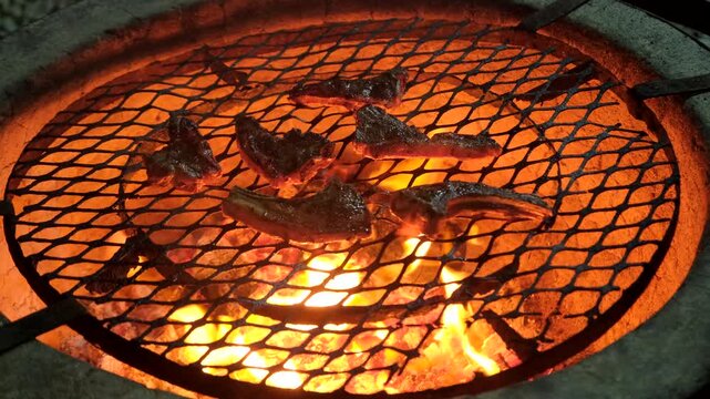 Sizzling lamb chops being grilled on hot coals of wood fire in round fire pit