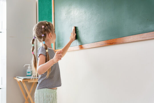 Young girl cleaning the chalkboard in a classroom, Elementary student erasing a green blackboard in school, Education concept, cute girl cleaning the whiteboard in a classroom environment
