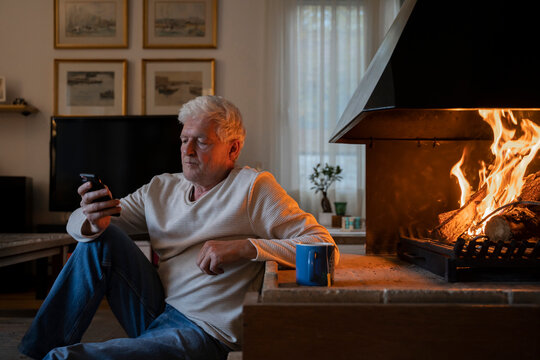 Senior man using mobile phone while sitting by fireplace at home
