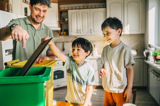 Smiling father teaching children to sort waste in the kitchen