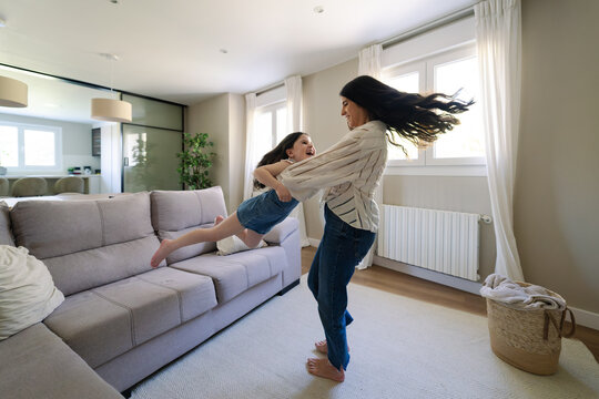 Mother and daughter spin and laugh playfully in the living room