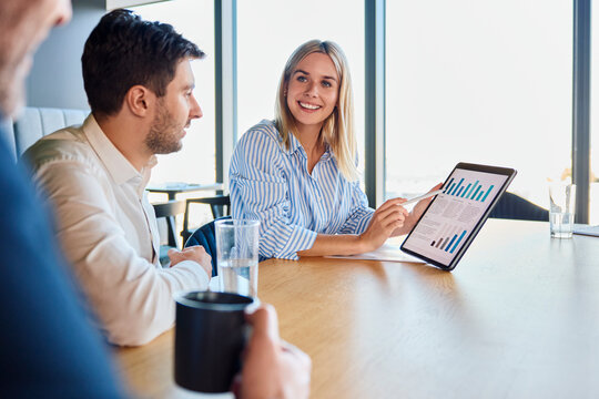 Happy young businesswoman discussing over graph with colleagues