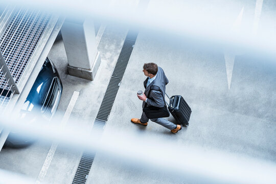 Top view of businessman walking with baggage and takeaway coffee at a car park