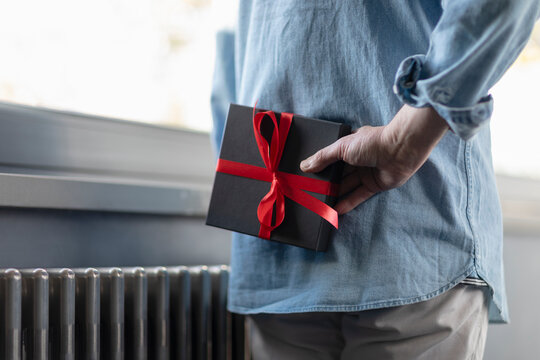 Man holding gift box behind while standing at home