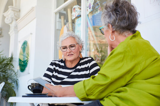 Friends use a digital tablet together at an outdoor cafe table