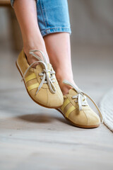 Naklejka premium Closeup of feet wearing beige lace sneakers with yellow stripes, rolled denim jeans, and relaxed casual styling on pale wooden floor in soft indoor light, neutral lifestyle fashion