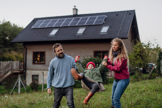 Happy parents holding hands and playing with daughter in front of house