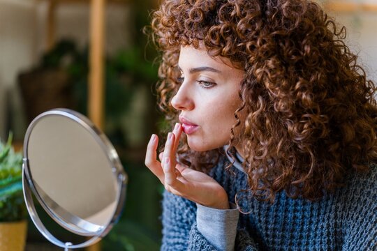 Woman checking reflection and touching lip during skincare routine at home