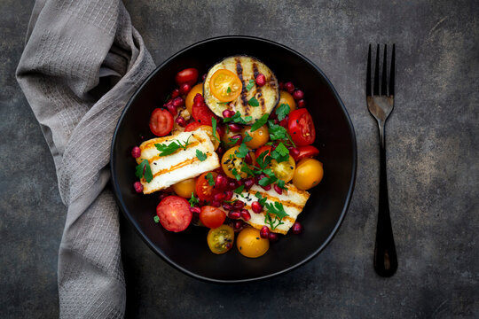 Bowl of Persian salad with tomatoes, grilled halloumi cheese, eggplant, pomegranate seeds, sumac, black sesame and parsley