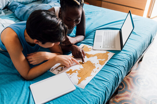 Young lesbian couple planning trip with map on bed at home