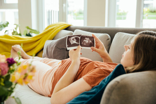 Pregnant woman looking at ultrasound scan while relaxing on the couch