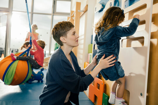 Pre-school teacher helping little girl climbing up a wall
