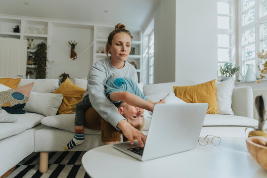 Mother taking care of boy while working on laptop at home